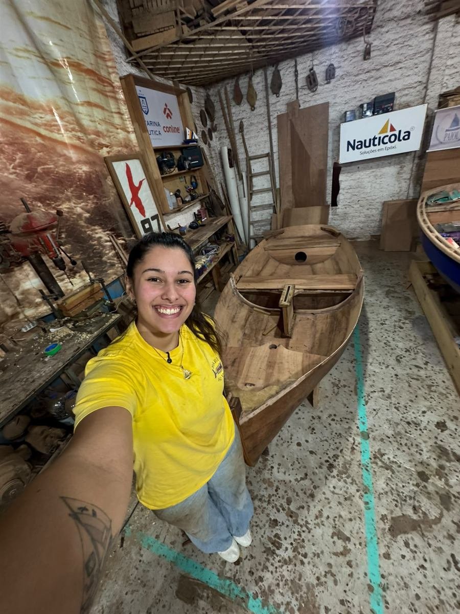 Maria sorrindo no estaleiro ao lado do casco de madeira do Albacora II